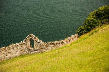 Deniz kıyısında, çim kaplı tepe yan ve eski taş duvar ile pencere açık havada, İrlanda