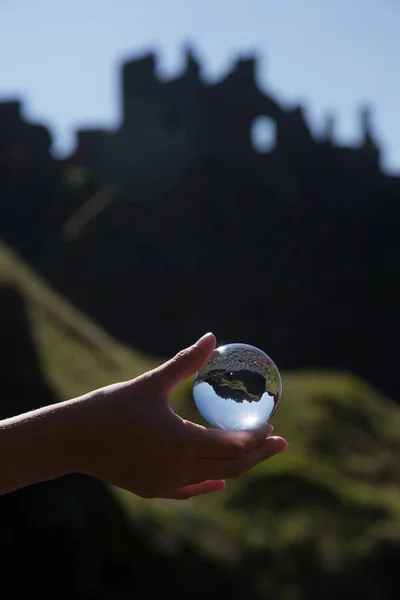 Glass ball in hand, ruins of old irish castle behind, Dunluc