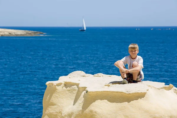 沿岸の岩、青い海の背景に金髪の子供の笑顔 — ストック写真