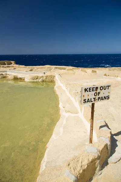 Velhas salinas abandonadas, um sinal de cautela enferrujado e horizonte sobre o mar na ilha de Gozo, Malta — Fotografia de Stock