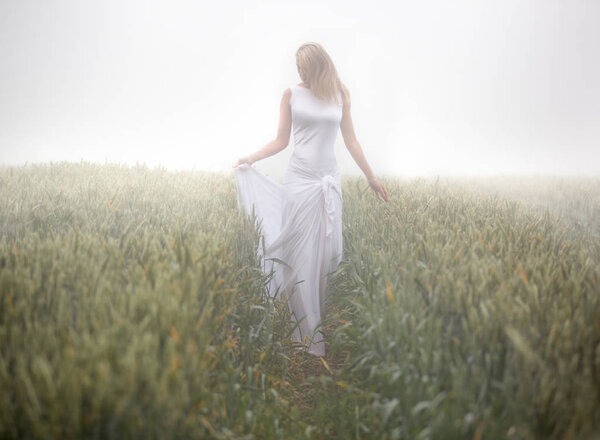Beautiful slim blonde woman plays in white dress, fogy meadow, outdoor