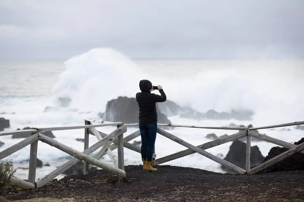 Wild, stormy weather, weavy ocean, rocky shore, wooden fence, woman in black look at the sea.