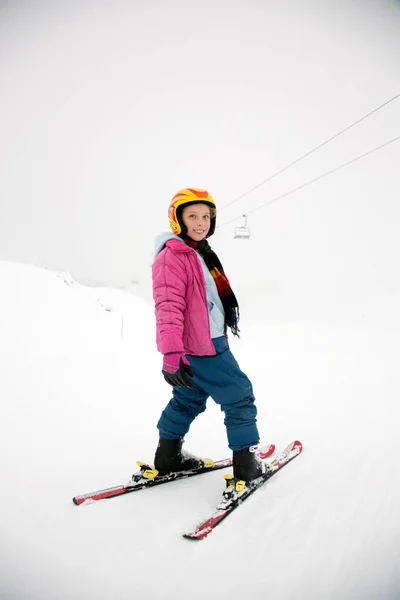 若いアクティブな女の子は黄色のヘルメットとピンクのコートに棒なしで下り坂の空 雪と霧の水で区切られた切り取り — ストック写真