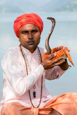 Portre çapkın yetişkin erkekte Türban ve göl kenarında oturan kobra. Pokhara, Nepal
