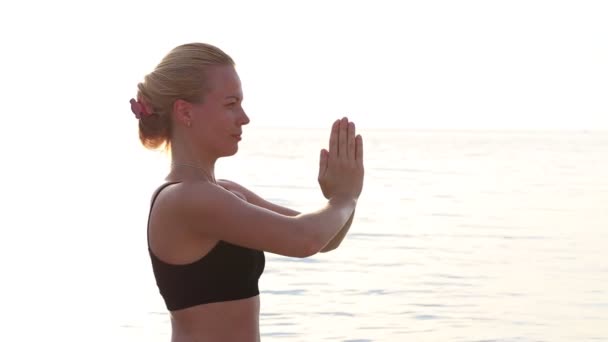 Glad ung kvinna utövar yoga på stranden vid solnedgången. — Stockvideo