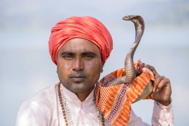 Portre çapkın yetişkin erkekte Türban ve göl kenarında oturan kobra. Pokhara, Nepal