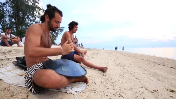Hombres tocando un instrumento llamado "Hang" o "Hang drum" al atardecer en la playa durante una fiesta de luna llena en la isla Koh Phangan, Tailandia — Vídeo de stock