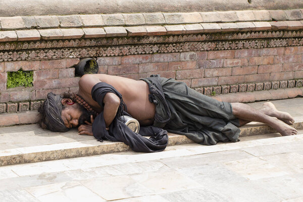 Бедный садху, святой человек, спящий на улице в храме Пашупатинатхи, Катманду. Непал
