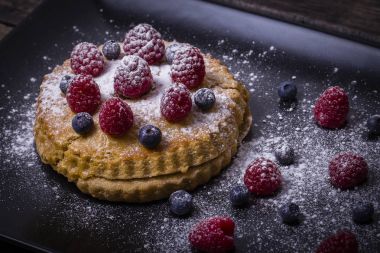 Kek ahududu, yaban mersini, deniz topalak serpilir ile pudra şekeri bir siyah plaka üzerinde