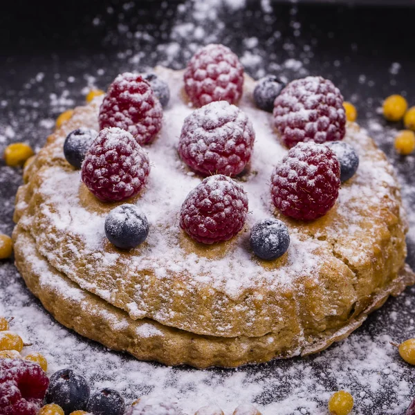 Kuchen mit Himbeeren, Blaubeeren, Sanddorn bestreut Puderzucker auf einem schwarzen Teller — Stockfoto