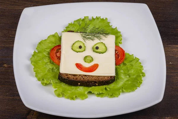 Cibo divertente per bambini - faccia sul pane, a base di formaggio, lattuga, pomodoro, cetriolo e pepe . — Foto Stock