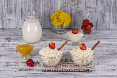 Süzme peynir, ekşi krema, süt, kırmızı çilek ve masanın üzerine bal