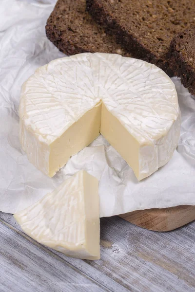 Brie tipo de queijo. Queijo Camembert. Queijo Brie fresco e uma fatia em uma tábua de madeira com fatia de pão preto. Italiano, queijo francês . — Fotografia de Stock