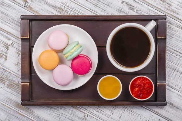 Kaffee, Honig, Erdbeermarmelade und Makkaronenkuchen auf einem Tablett auf einem weißen Holztisch. Lifestylekonzept — Stockfoto
