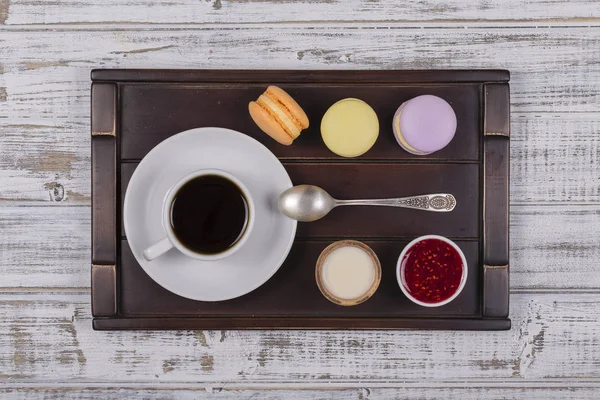 Cup of coffee, spoon and macaron cakes on tray on white wooden table. Lifestyle concept. Top view — Stock Photo, Image