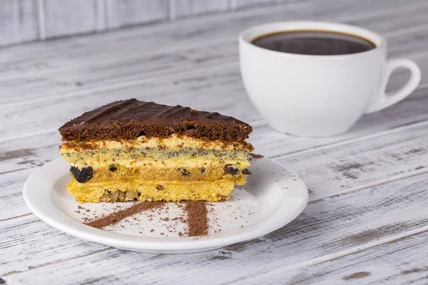 Chocolate piece of cake from biscuit dough with poppy seed, prune and walnuts and cup of coffee — Stock Photo, Image