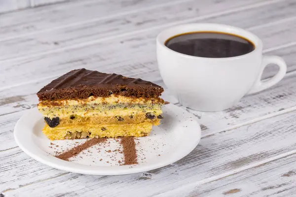 Chocolate piece of cake from biscuit dough with poppy seed, prune and walnuts and cup of coffee — Stock Photo, Image