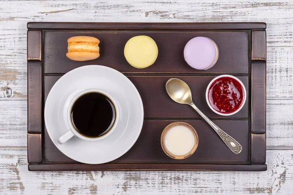 Xícara de café, colher e bolos de macaron na bandeja na mesa de madeira branca. Conceito de estilo de vida. Vista superior — Fotografia de Stock