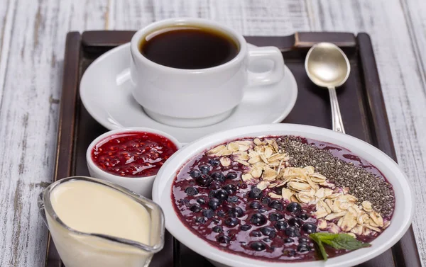 Kopp kaffe och müsli gjord av blåbär, chiafrön, havre flingor med yoghurt på en bricka på vita träbord. Livsstilskoncept. Närbild, ovanifrån — Stockfoto