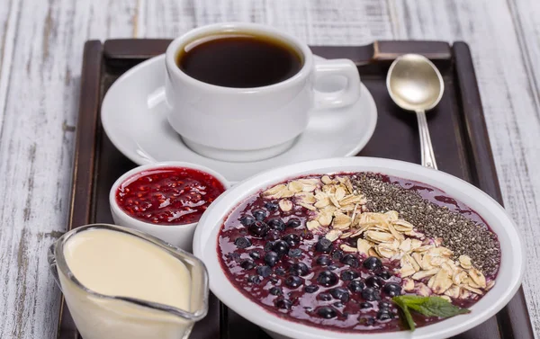 Xícara de café e muesli feito de mirtilo, sementes de chia, flocos de aveia com iogurte em uma bandeja na mesa de madeira branca. Conceito de estilo de vida. Fechar, vista superior — Fotografia de Stock