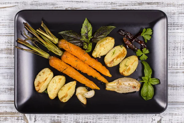 Patatas jóvenes, zanahorias, cebollas, pimientos, ajo cocido en el horno en el plato negro. Vista superior —  Fotos de Stock