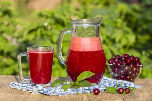 Dietary detox drink with red cherry in clear water with ice. Cherry juice in jug and in glass and ripe cherries in plate — Stock Photo, Image
