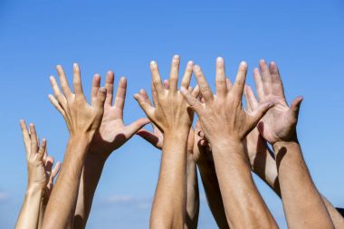Group raising hands against blue sky background clipart