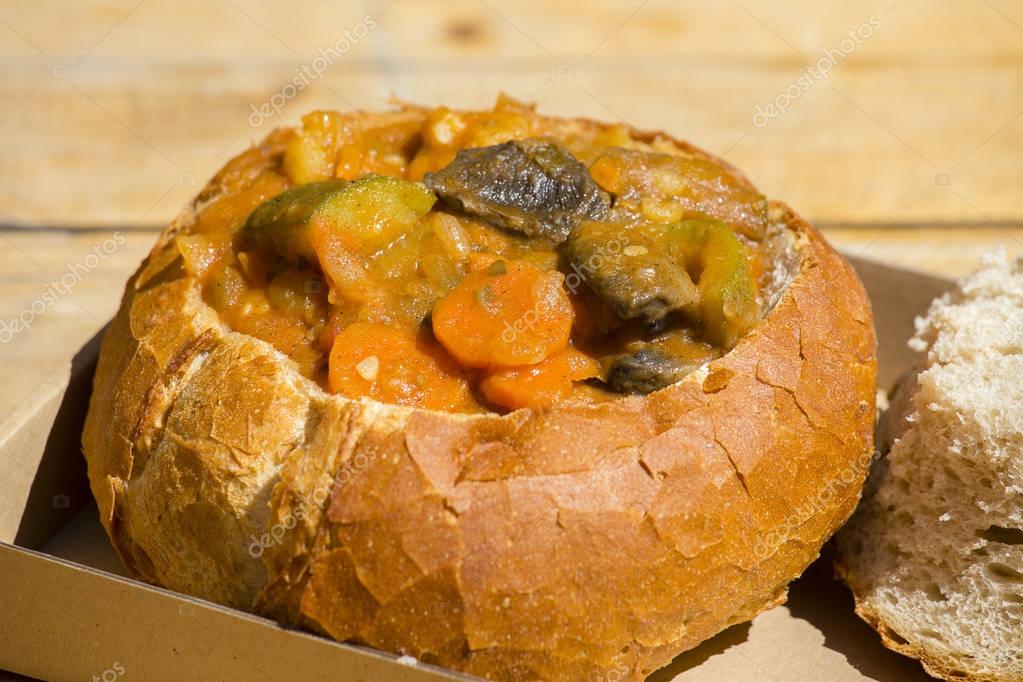 Goulash soup in bread served in a bread bowl . A dish of Hungarian