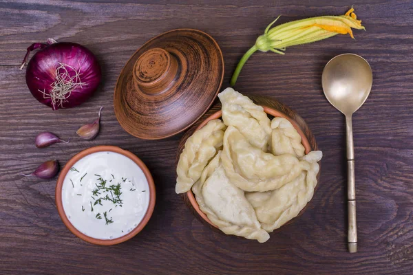 Ukrainian and Russian dishes - vareniki or dumplings with mashed potatoes or cottage cheese in clay pot on a wooden background