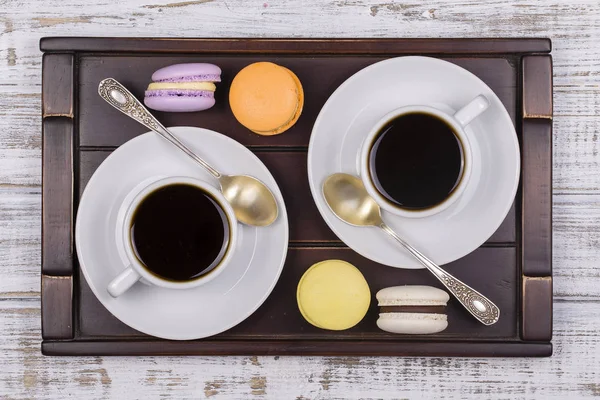 Two cups of coffee, spoon and macaron cakes on tray on white wooden table. Lifestyle concept. Top view — Stock Photo, Image