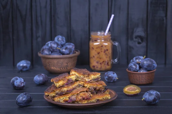 Hemmagjord plommon paj i plattan, plommon smoothies och rå plommon på svart trä bakgrund — Stockfoto