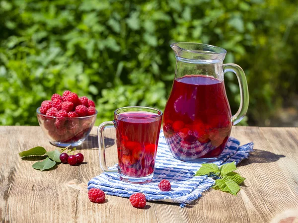 Red compote with cherry, strawberry, gooseberry and raspberry on wooden table in nature — Stock Photo, Image