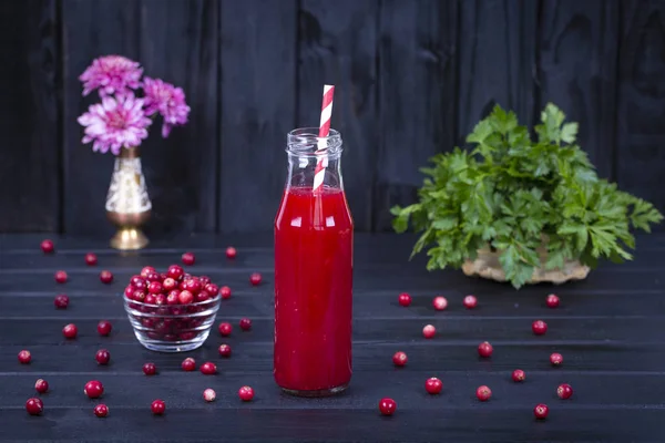 Bir cam şişe ve siyah ahşap arka plan üzerinde ham kızılcık kızılcık suyu kapat