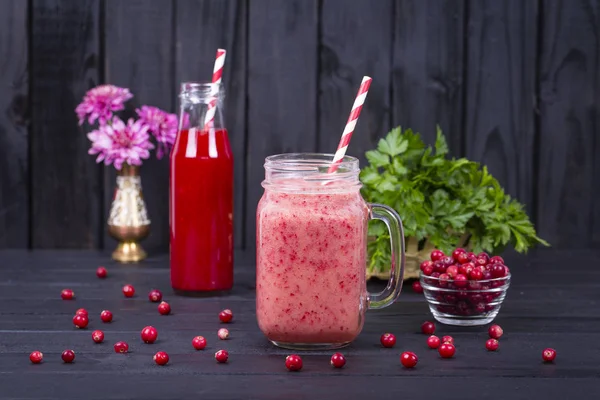 Cranberry juice smoothie shake in glass mug and raw cranberry on black wooden background, close up — Stock Photo, Image