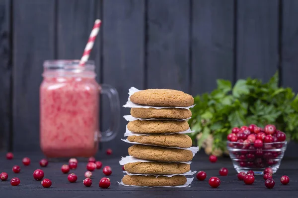 Oat cookies, cranberry juice smoothie and raw cranberry on black wooden background, close up