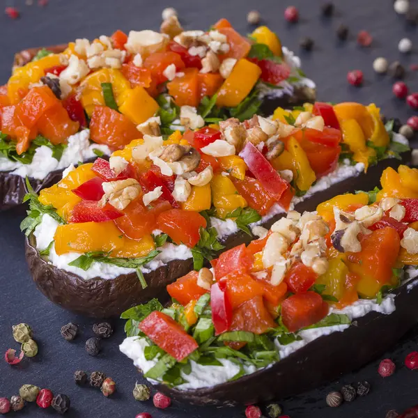 Berenjenas al horno rellenas de verduras, nueces y queso crema sobre un fondo de pizarra negra, de cerca —  Fotos de Stock