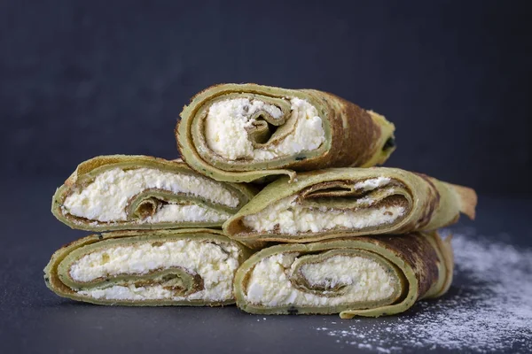 Homemade pancakes with green spirulina stuffed white cottage cheese with raisins on a black slate background, close up — Stock Photo, Image