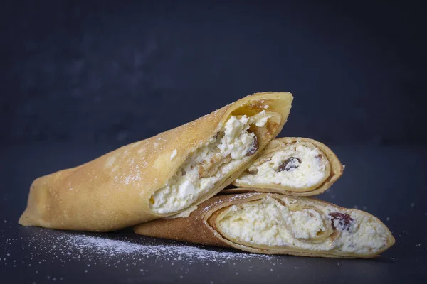 Panqueques caseros rellenos de requesón blanco con pasas sobre un fondo de pizarra negra, de cerca — Foto de Stock