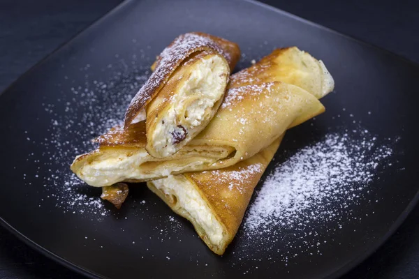 Hausgemachte Pfannkuchen gefüllt mit weißem Quark und Rosinen auf einem schwarzen Teller, Nahaufnahme — Stockfoto