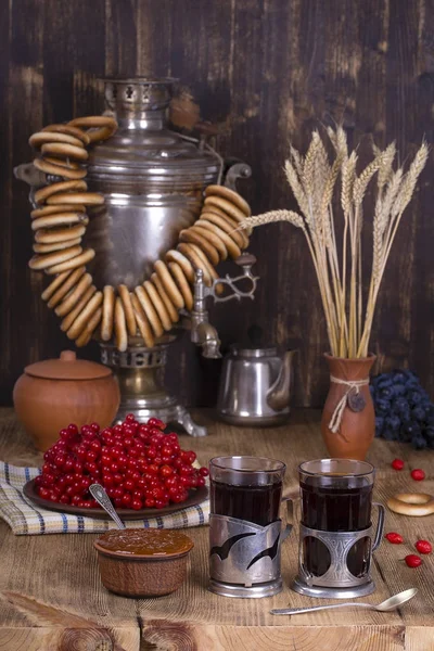 Russische traditionele waterkoker Samowar op de houten tafel. Zwarte thee, bagels, rode viburnum, jam en Russische Samowar in de rustieke stijl. — Stockfoto