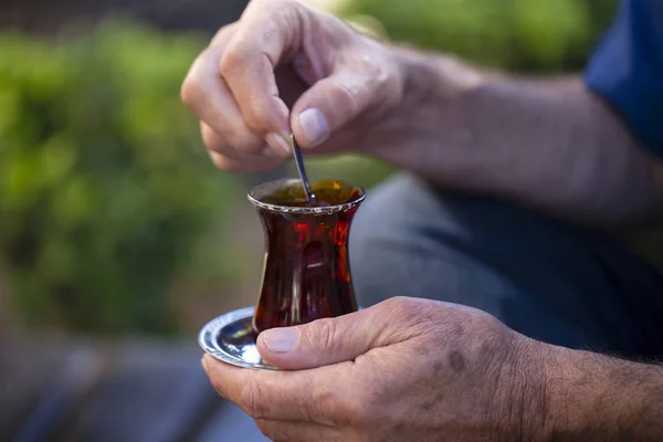 Delicioso chá turco vermelho com vidro tradicional em forma de pêra com uma colher de chá na mão do homem — Fotografia de Stock