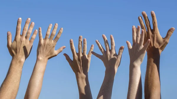 Group raising hands against blue sky background — Stock Photo, Image