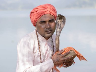 Türban ve göl kenarında oturan kobra yılan oynatan kimse yetişkin adam portresi. Pokhara, Nepal