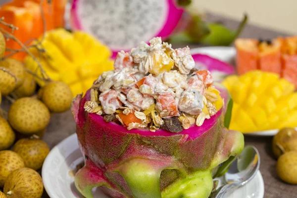 Insalata di frutta tropicale fresca con fiocchi d'avena, uvetta, noci, yogurt e miele nella buccia di frutta del drago, da vicino — Foto Stock