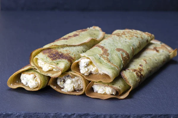 Oekraïense gerechten - huisgemaakte pannenkoeken met groene spirulina gevulde witte kwark met rozijnen op een zwarte leisteen achtergrond — Stockfoto