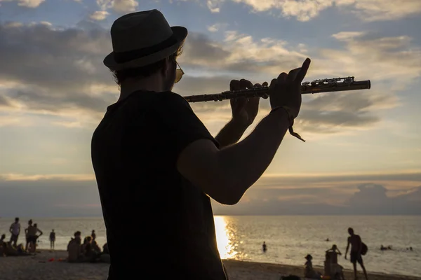 Muzikant man spelen de fluit bij zonsondergang op het strand tijdens een volle maan partij in eiland Koh Phangan, Thailand — Stockfoto