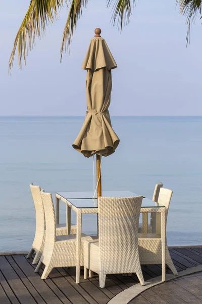 Mesa blanca y sillas de ratán en la cafetería vacía junto al agua de mar en la playa, Tailandia . —  Fotos de Stock