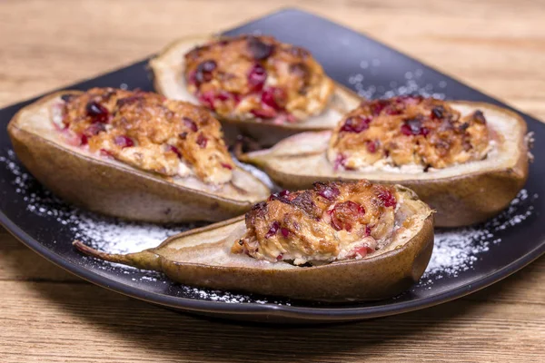 Pere al forno fatte in casa con ricotta, miele, mirtilli rossi e noci in piatto nero su sfondo di legno, cibo sano — Foto Stock