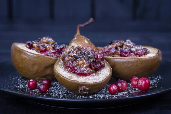 Hausgemachte gebackene Birnen mit Honig, roten Preiselbeeren und Walnüssen im Teller auf schwarzem Holzhintergrund, gesunde Ernährung — Stockfoto