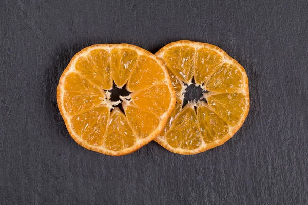 Dos rebanadas de mandarina se encuentran en pizarra negra. Concepto de alimentos saludables, orgánicos, veganos, vitaminas. Vista superior. Naranja fresco, fondo de mandarina — Foto de Stock